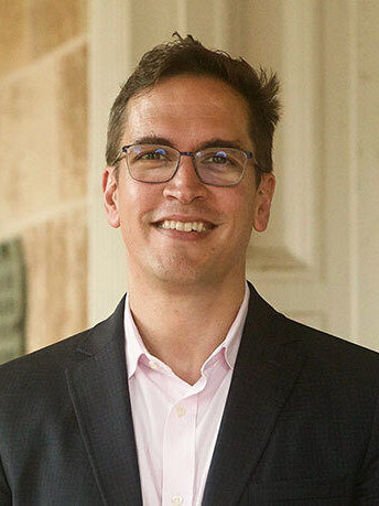 Picture of Associate Dean Grant Nelsestuen. He has short brown hair and is wearing a pink button down shirt with a black jacket.