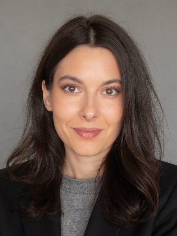 Headshot of Annette Zimmermann. She has long, straight, brown hair, and is wearing a gray shirt with a black jacket.