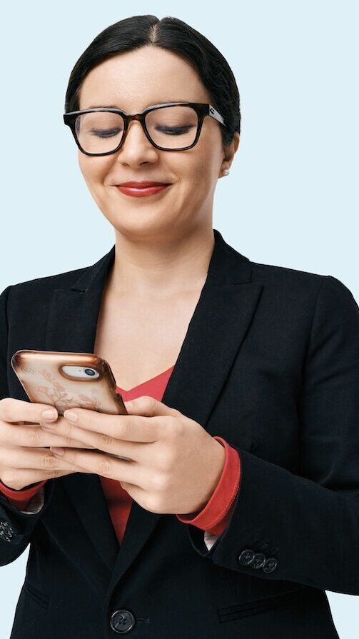 Headshot of Catalina Toma. She has black, straight hair styled in a low bun, and is wearing glasses, a red undershirt, and a black jacket. She is looking at an iPhone with a case decorated in flowers.