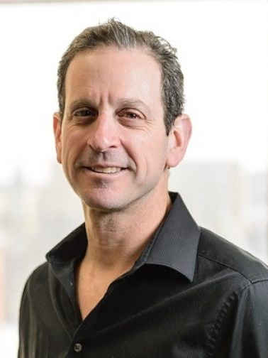 Headshot of Russ Castronovo. He has short black and gray hair, and is wearing a black button down shirt.