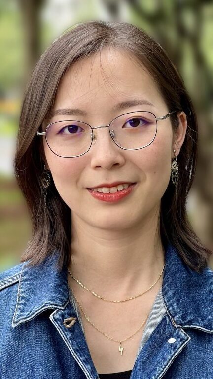 Headshot of Lucy Quanxin Yang. She has shoulder-length straight black hair, and is wearing glasses, earrings, two gold necklaces, and a denim jacket.